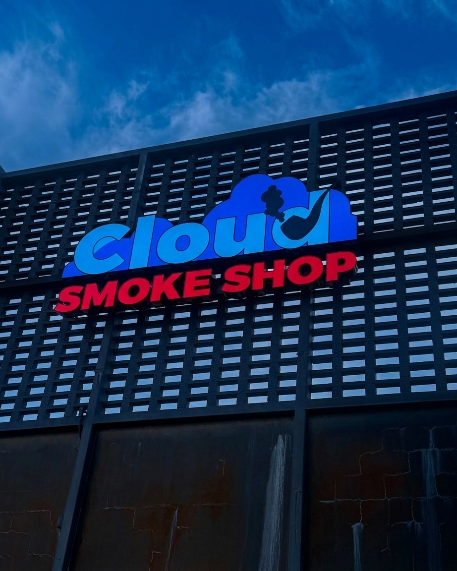 Cloud Smoke Shop's blue and red storefront sign mounted on the store's dark facade under an open Tallahassee sky.